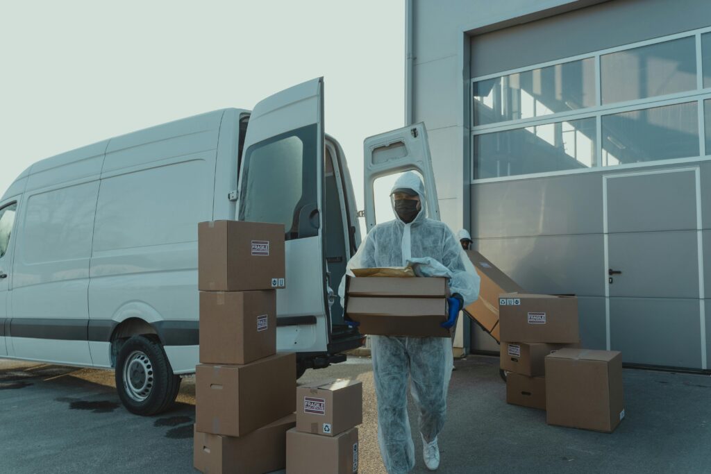A delivery worker in PPE unloads boxes from a van. Efficient and safe logistics.